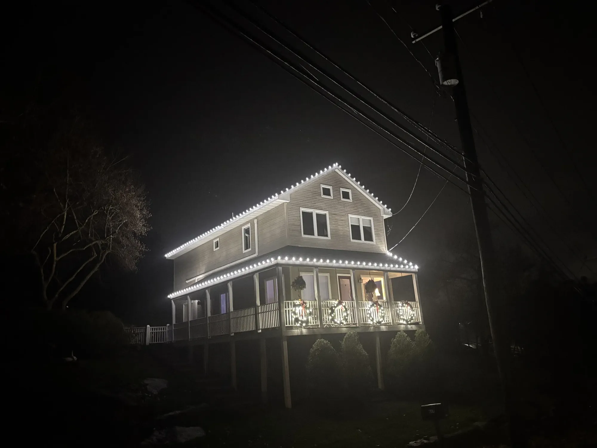 Hillside home with lit rooflines and wreaths on every section of the porch railing