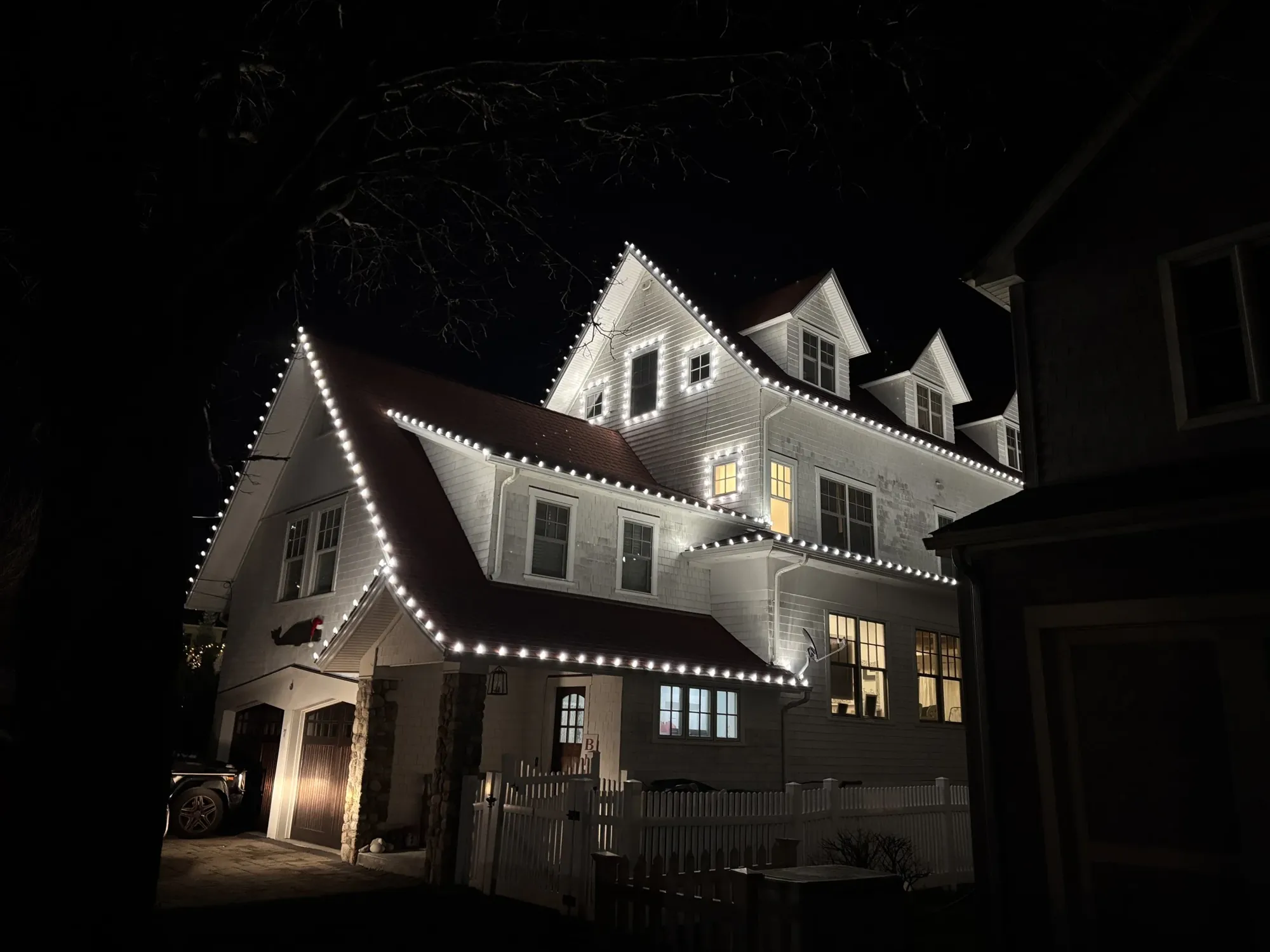 Shingle-style home with warm white lights along every roofline, dormer and window, installed by Illuminex